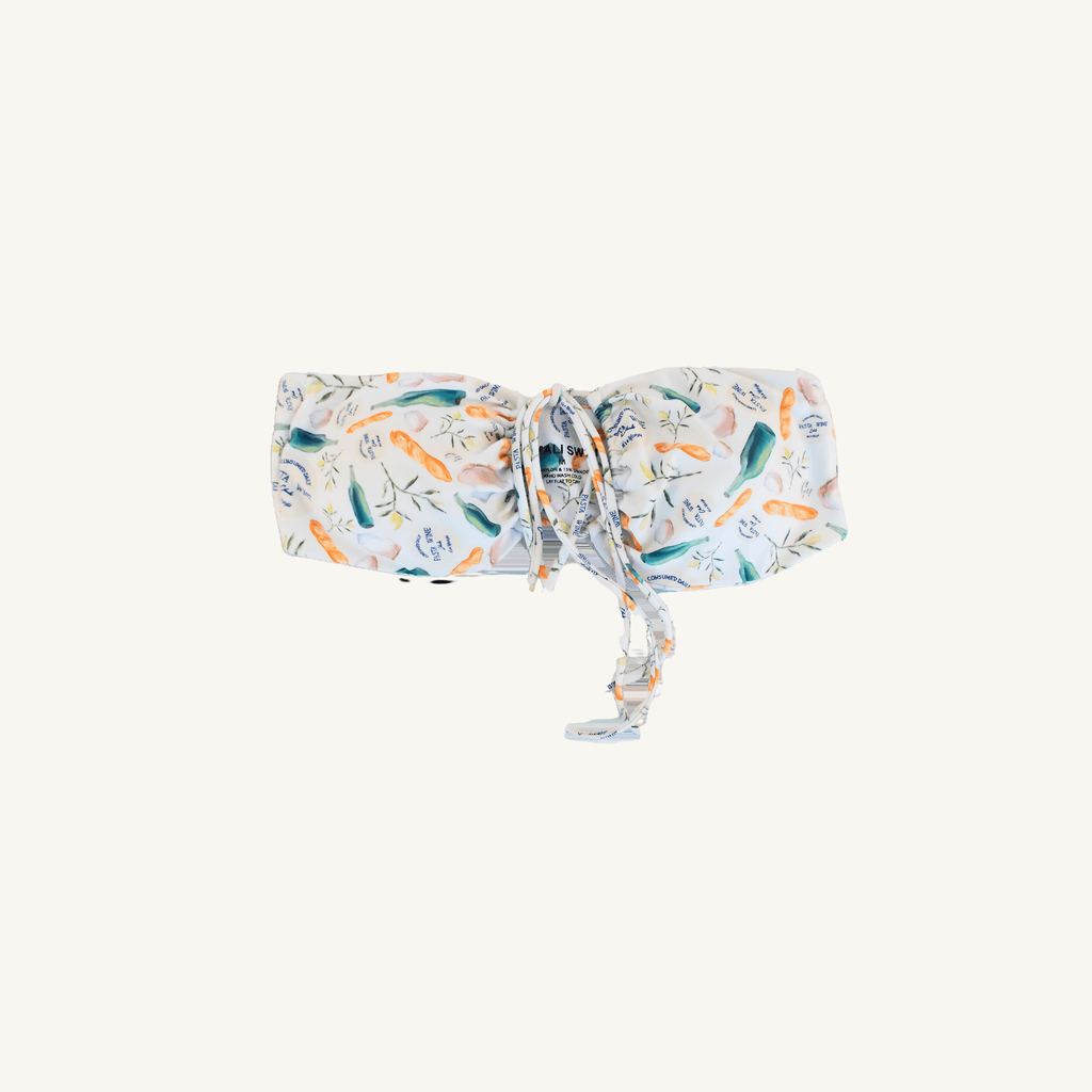 A stylish white bandeau bikini top featuring a colorful print of various vegetables and herbs, accented with text elements, and designed with a front tie detail for adjustable fit and trendy beachwear appeal. | PicSEO 1778548962890